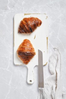 Top view of crispy croissant on white serving board on marble background
