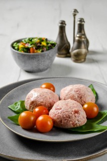 Semifinished frozen veal meatballs on a plate with basil and tomato
