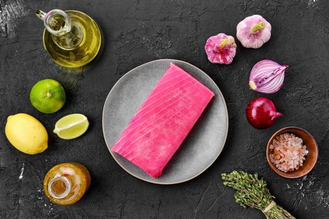 Top view of raw tuna fillet in plate with spice on black background