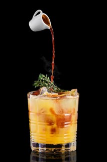 Pouring hot espresso in glass with tonic and orange syrup and thyme on black background