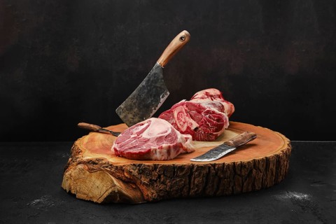 Chopping ossobuco steak from beef shank with cleaver on wooden stump