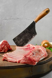 Raw whole rack of lamb on wooden slab with butcher cleaver