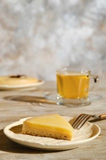 Piece of lemon tart with tea under direct sunlight with hard shadows on the table
