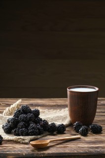 Heap of fresh dewberry on sackcloth table-napkin and clay cup with milk on wooden table