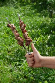 Hand with thumb up holding skewer with shashlik