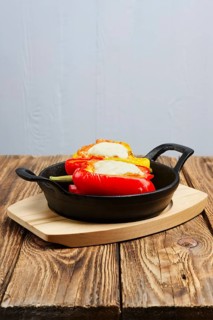 Bell pepper stuffed with meat with melted cheese mozzarella on top baked in oven in cast iron skillet. Top view. Natural wooden background