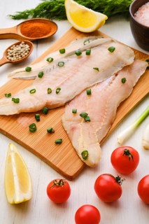 Raw fresh haddock fillet on wooden cutting board with spice and herbs