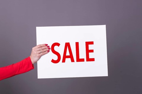 Female hand holding a Sale poster. Studio shot