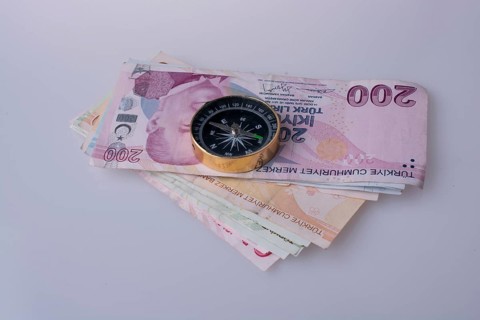 Turkish Lira banknotes by the side of a compass on white background