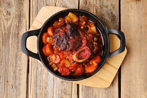 Overhead view of cast iron skillet with ossobuco on wooden table
