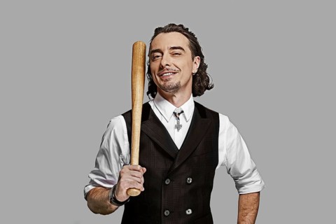 Dramatic man in white shirt and black vest with long curly hair holding baseball bat