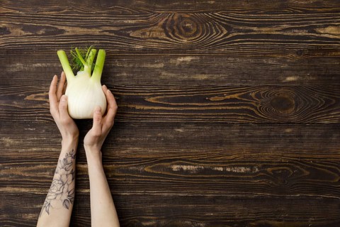 Overhead view of fresh fennel bulb in hands over wooden background