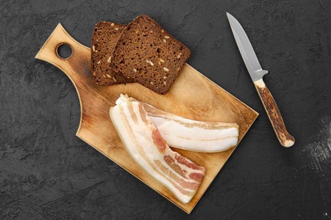 Top view of two slices of bacon and brown bread on wooden cutting board