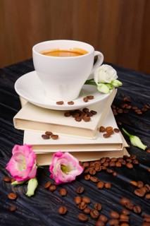 Cup of coffee on top of pile of books with coffee beans and flowers scattered on the table