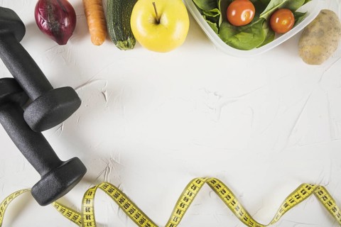 Overhead view of measuring tape food and dumbbell on white backdrop
