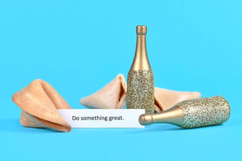 Open fortune cookie with motivational text saying 'Do something great' with golden champagne bottles