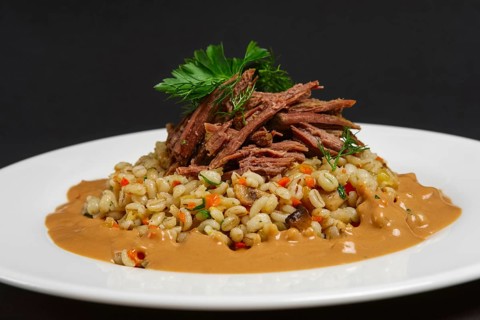 Plate with boiled beef and pearl barley on black background