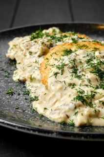Closeup view of potato patty with fried boletus and creamy sauce on a plate