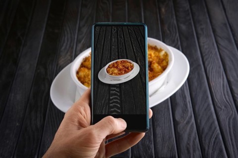 Hand with phone. Blogger making photo of food. Pasta baked with shrimps and cheese