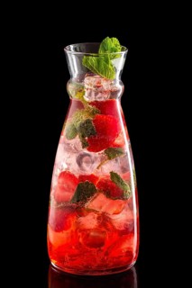 Pitcher with strawberry and mint ice lemonade isolated on black background