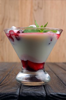 A glass of youghurt with marshmallow and raspberries decorated with mint leaves