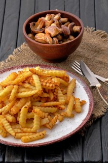 Fried crinkle cut american fries and roasted mushrooms on dark wooden table