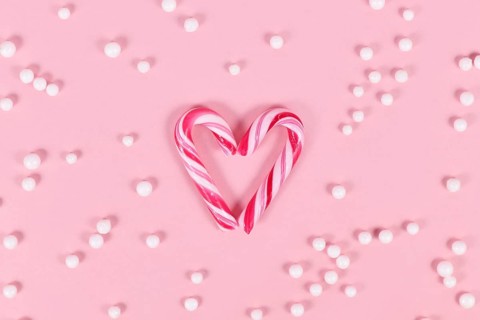 Small striped Christmas candy cane sweets forming heart on pink background