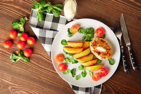 Fried chicken cutlet with potato slices served with tomato cherry and corn salad. Traditional belorussian food