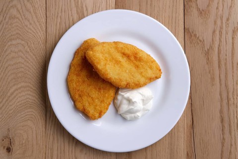 Top view of potato cutlet in breading stuffed with ham served with sour cream on wooden table