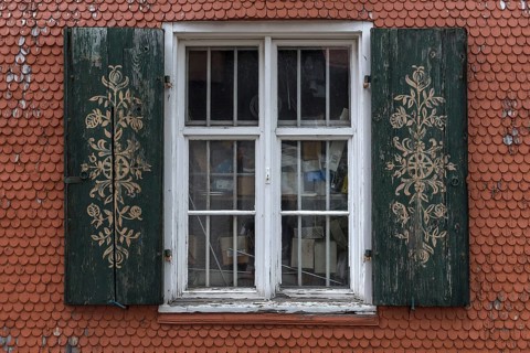 Ornate shutters on a barred window on a shingle facade