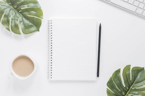 Notebook near coffee cup keyboard table with green leaves