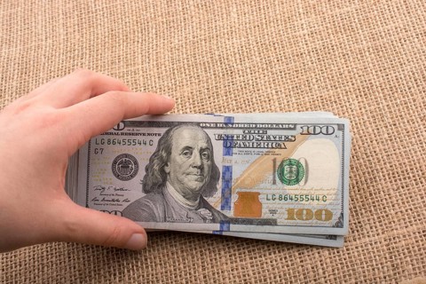Hand holding banknote bundle of US dollar on a linen canvas background