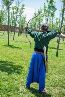 Archer with bow in traditional clothes shooting an arrow