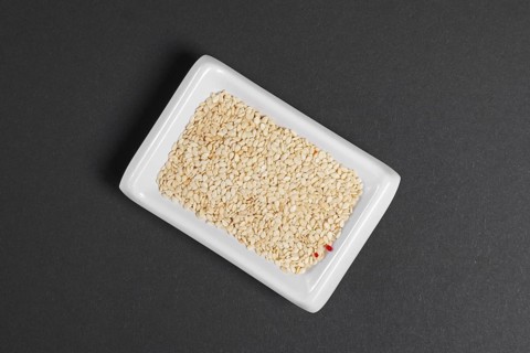 Top view of white sesame seeds in a little dish on gray paper