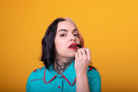 Beautiful caucasian woman applying a bright red color lipstick on her lips over yellow background