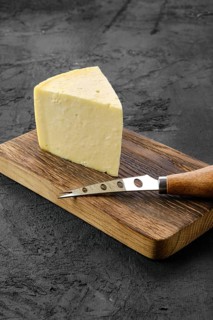 Triangular piece of hard cheese on wooden cutting board