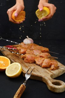 Pouring orange and lemon juice on skewers with raw turkey meat with sweet and spicy rub on dark background