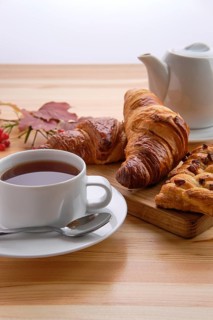 Puff pastry raisin bun and crispy croissant on wooden table with tea