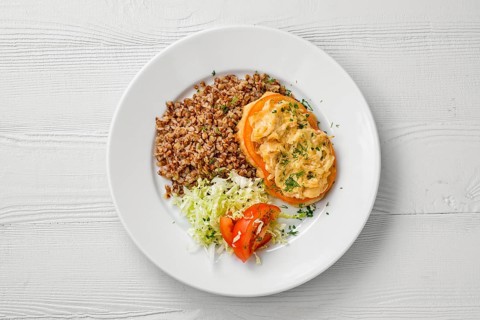 Top view of plate of chopped meat backed with tomato with buckwheat and cabbage salad