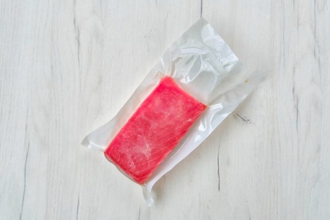 Raw frozen tuna fillet in vacuum packaging on wooden background