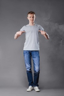Middle age man in jeans pointing fingers to his t-shirt on gray background