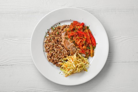 Top view of plate with chopped meat backed with bell pepper with buckwheat and cabbage salad
