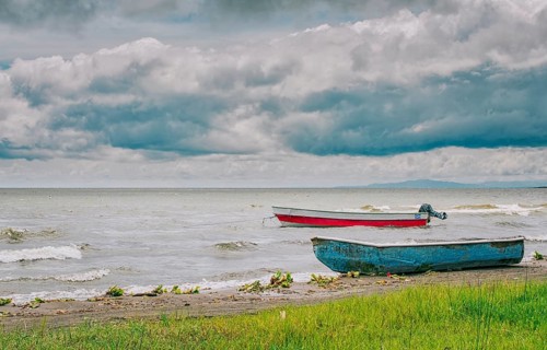 Two wooden fishing boats on the shore of a beautiful lake. Two fishing boats parked on the shore of a lake
