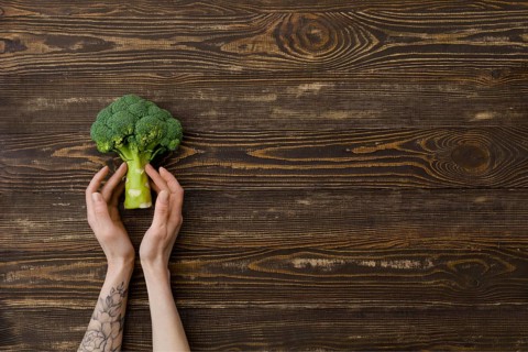 Overhead view of fresh broccoli in hands over wooden background