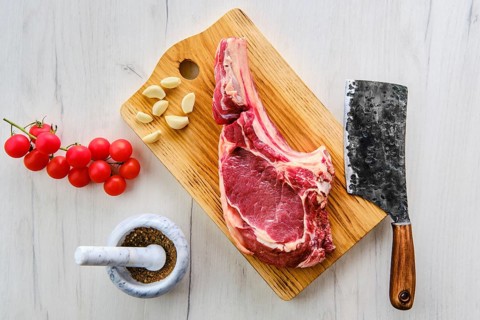 Beef ribeye steak bone-in with spice on wooden cutting board