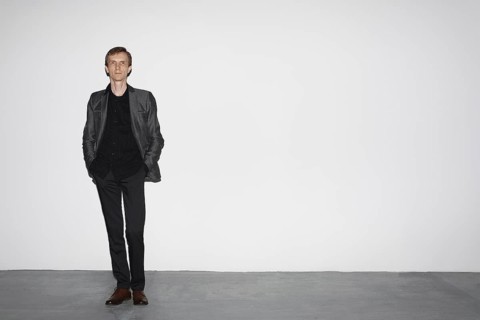 Man in wool jacket standing near white concrete wall with hands in pocket