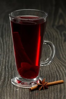 Glass of hot cherry tea with cinnamon on wooden table on dark wooden table