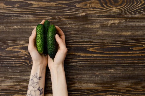 Overhead view of fresh cucumbers in hands over wooden background