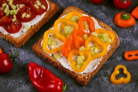 Slice of healthy whole grain toast topped with vegetables like yellow and orange bell peppers