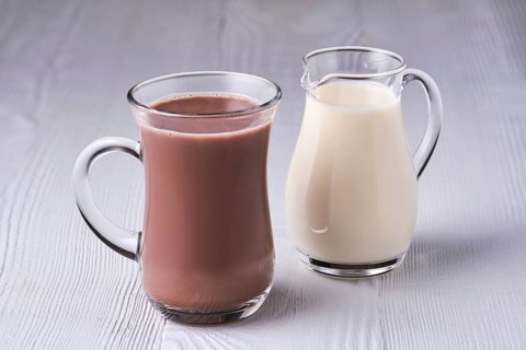 Cup of cappuccino and small creamer on wooden table
